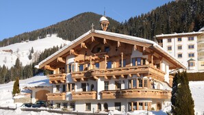 Un grand chalet en bois doté de nombreux balcons, avec un télésiège visible en arrière-plan.