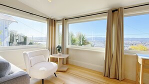 A modern room with a large window, a white chair, a small table with a plant, and a view of a cityscape. - StayAU 2BR Home w/ Stunning Views in Tasmania (Trevallyn)