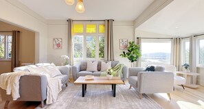 A modern living room with a grey sofa set, a wooden coffee table, and a view of greenery through large windows.