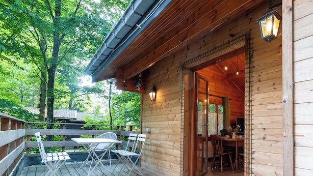 Une cabane en bois avec une terrasse, une table et des chaises, et une porte donnant sur l’intérieur.