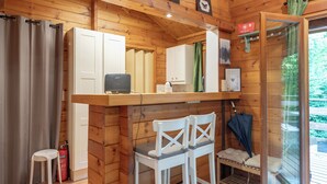 L’intérieur d’une cabane en bois comprend un coin cuisine, deux tabourets de bar blancs, un extincteur et une porte en verre donnant sur l’extérieur.