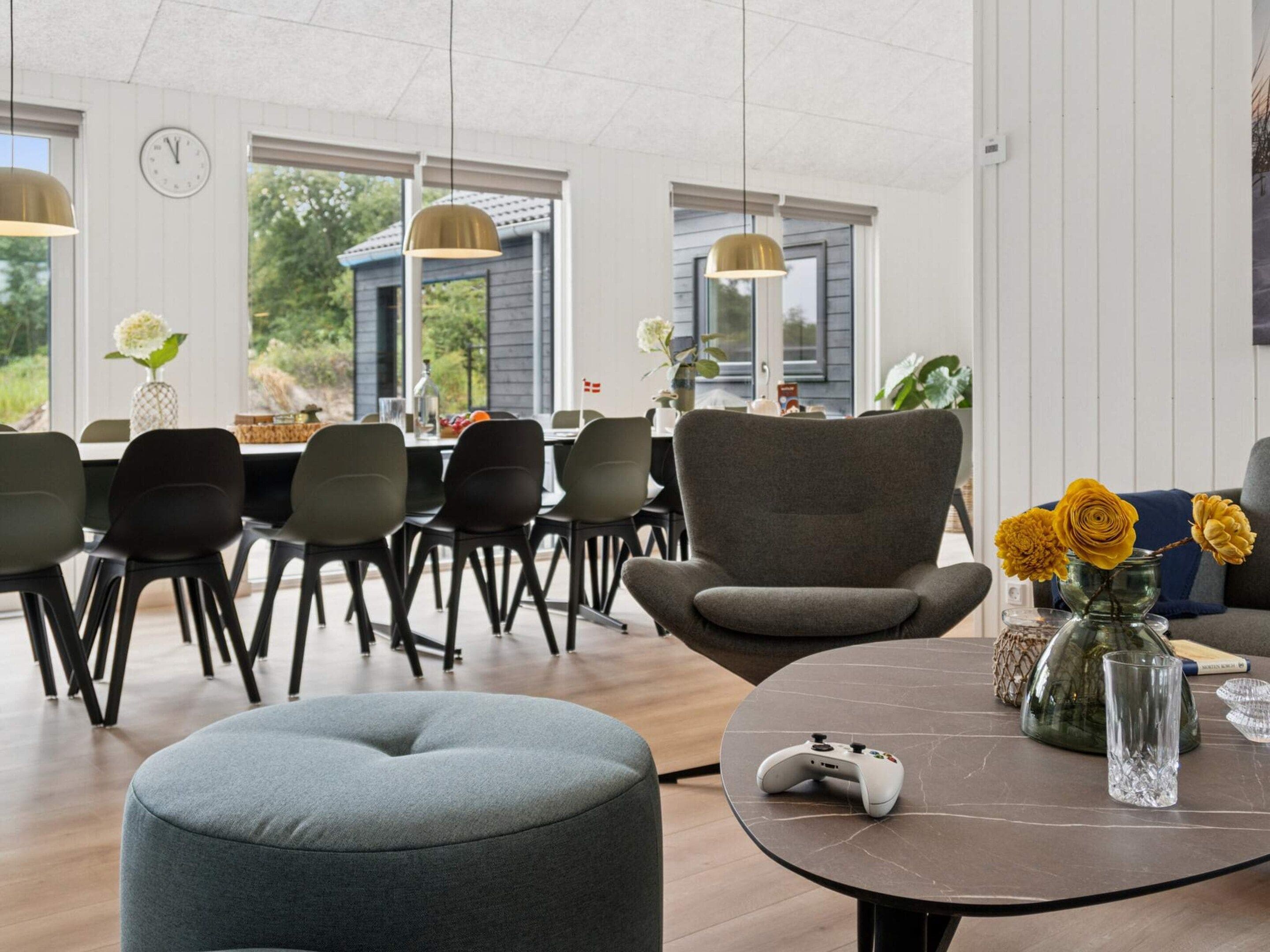 A modern living room with a grey ottoman, a gaming console on a marble table, and a vase with yellow flowers.