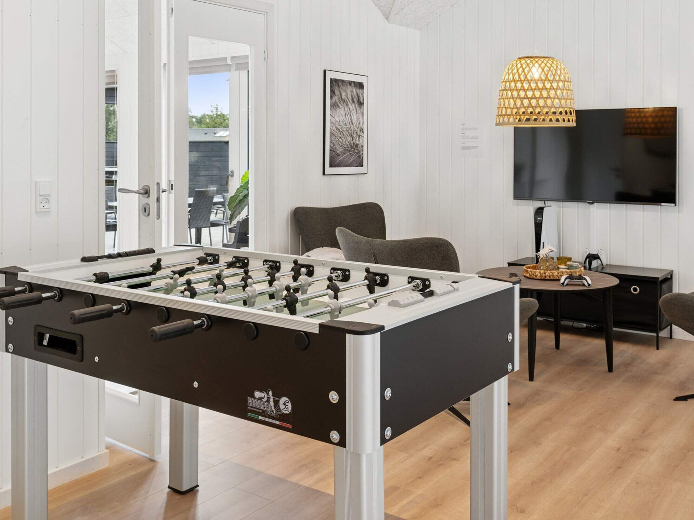 A modern living room with a foosball table, a comfortable seating area, a television, and a decorative lamp.