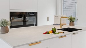 Una cocina moderna con armarios blancos, un horno negro, un grifo dorado y una ventana con vistas.
