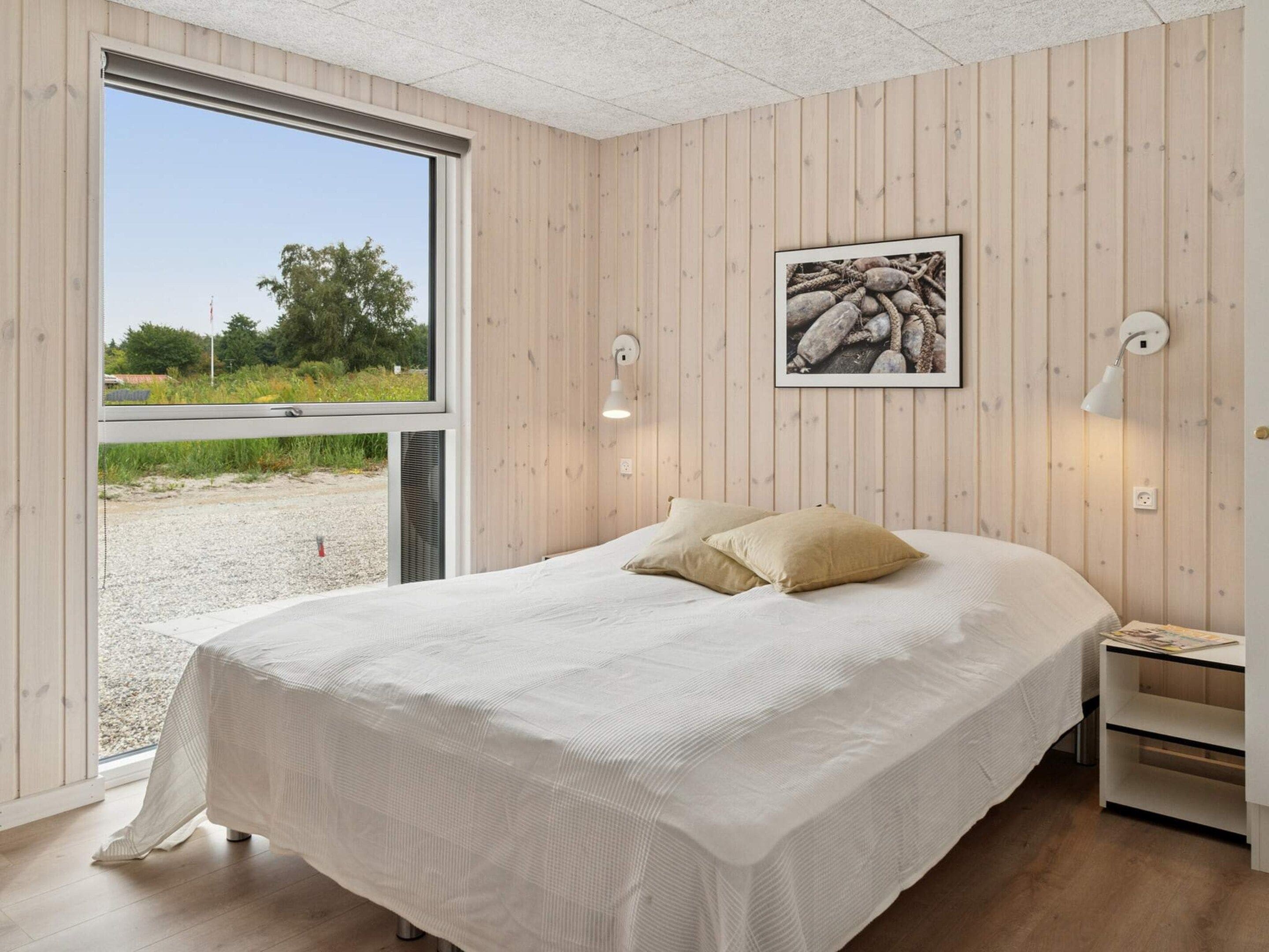 A bedroom with a large bed, wooden walls, a window, and a framed picture on the wall.