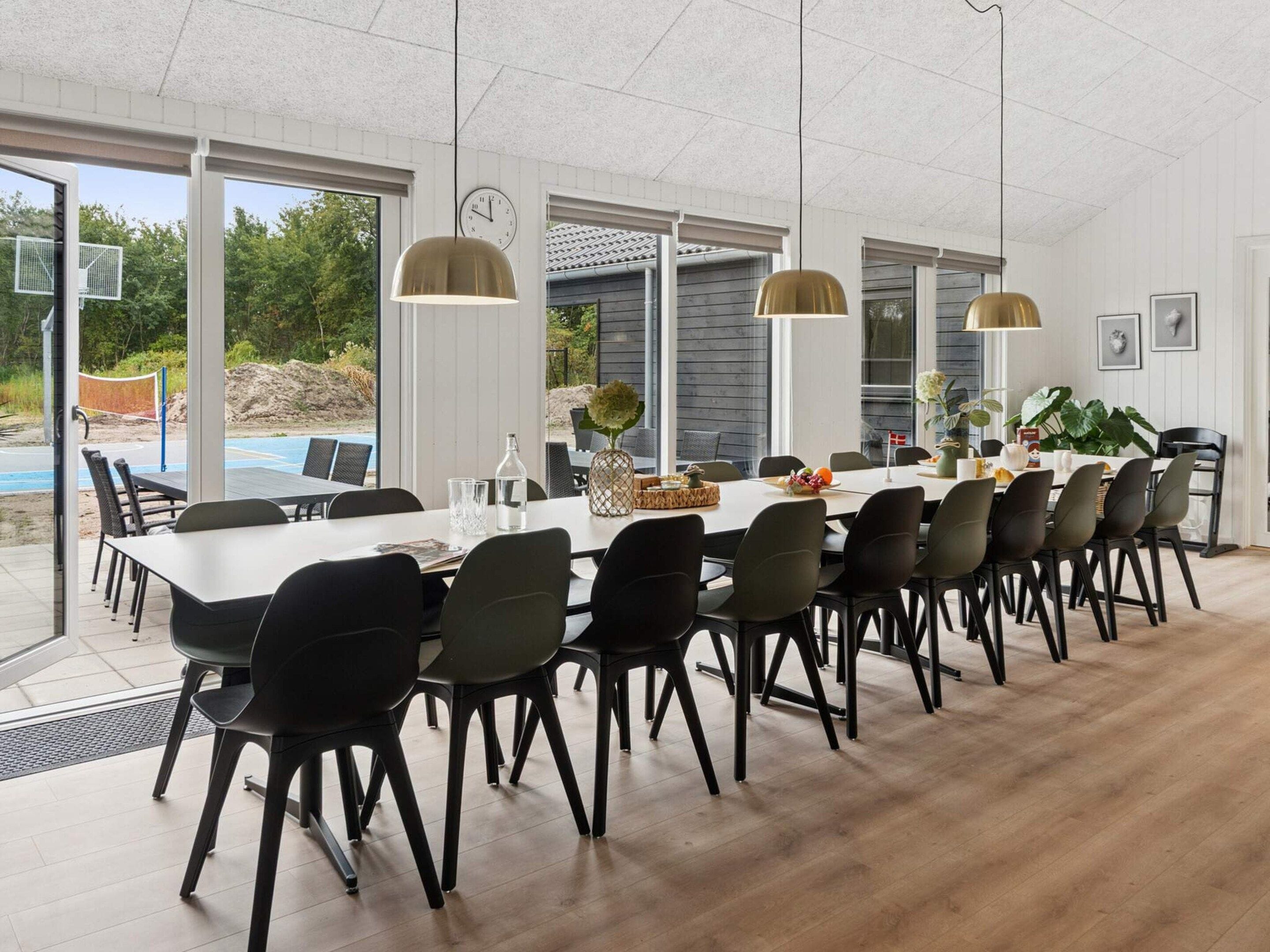 A dining area with a long table, chairs, pendant lights, and a view of the outdoors.