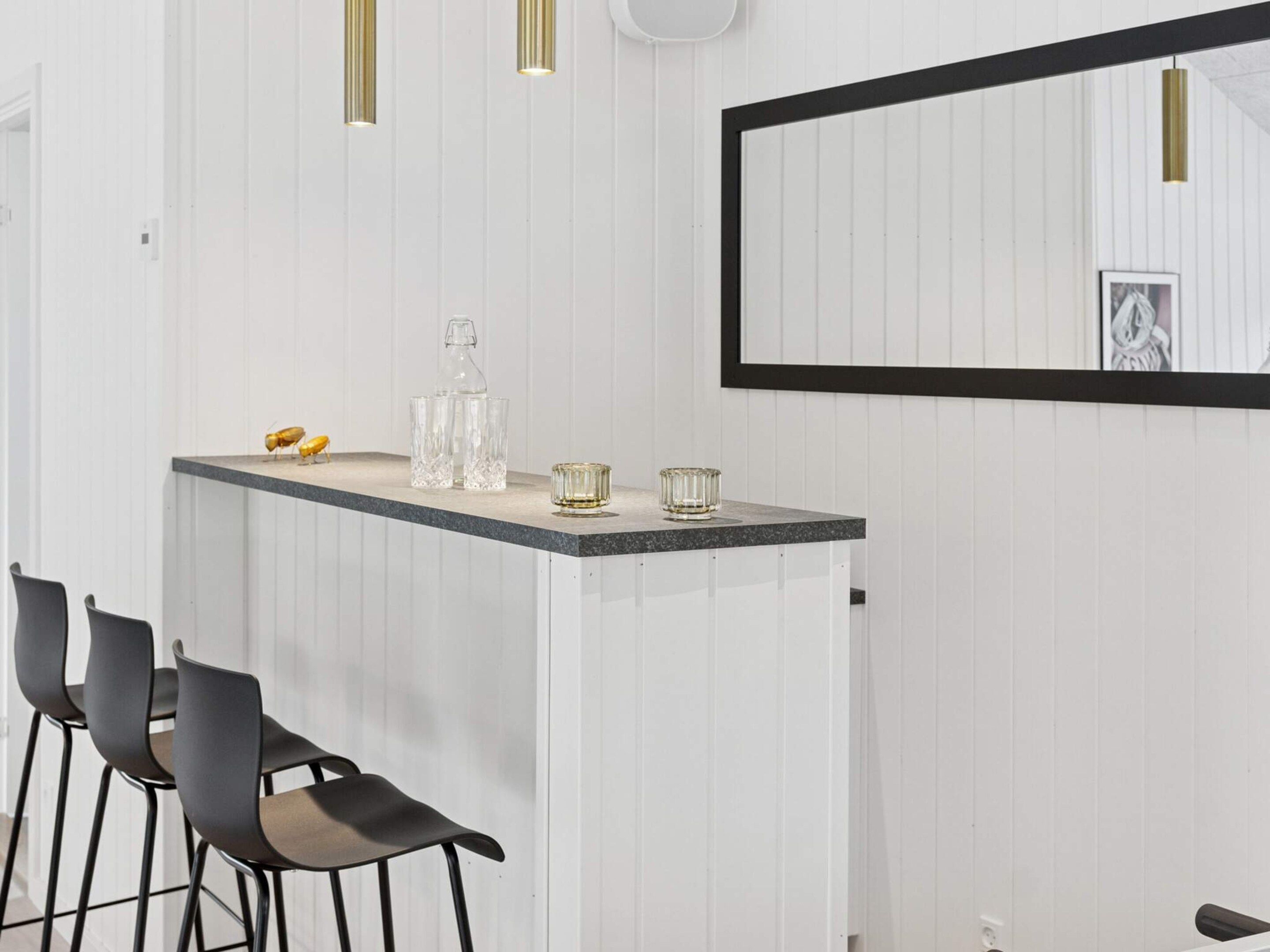 A bar area with a countertop, bar stools, a mirror, and pendant lighting.
