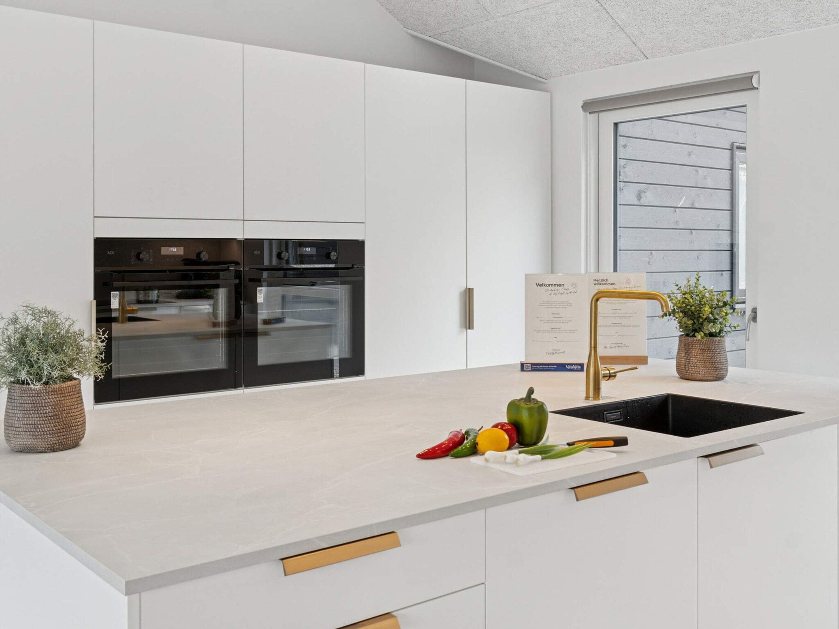 Una cocina moderna con armarios blancos, un horno doble, un lavamanos y una ventana con vistas.