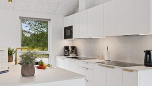 Una cocina moderna con armarios blancos, una cafetera Bosch negra y un ventanal con vistas a la vegetación.