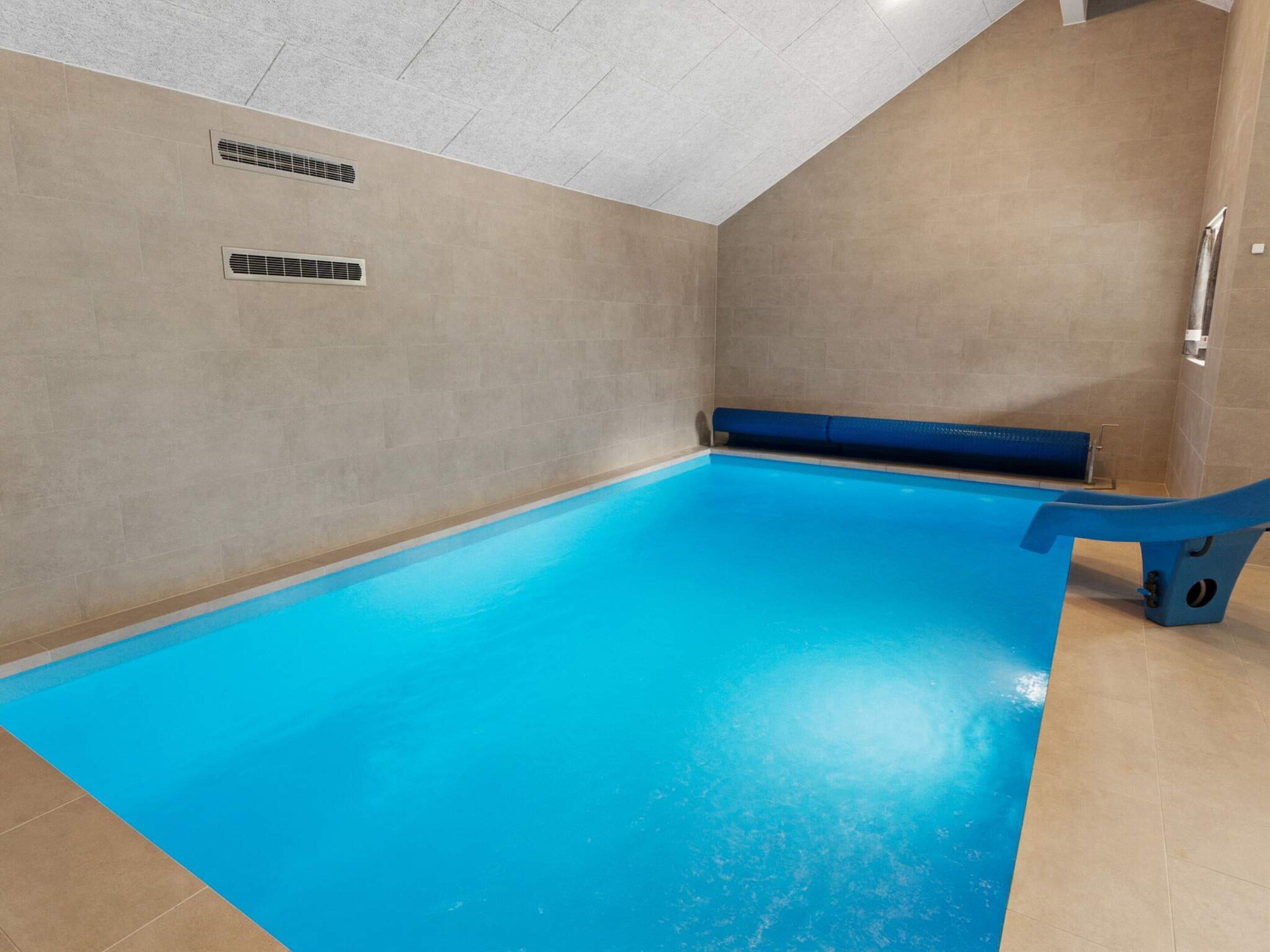 A swimming pool with a blue floor, a blue bench, and a wall-mounted handrail.