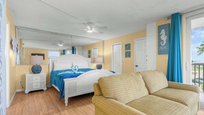 Un dormitorio con cama, sofá, ventilador de techo, espejo y puerta.