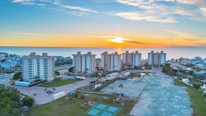 Un complejo residencial de edificios altos con varios pisos, un estacionamiento y vista al océano al atardecer.