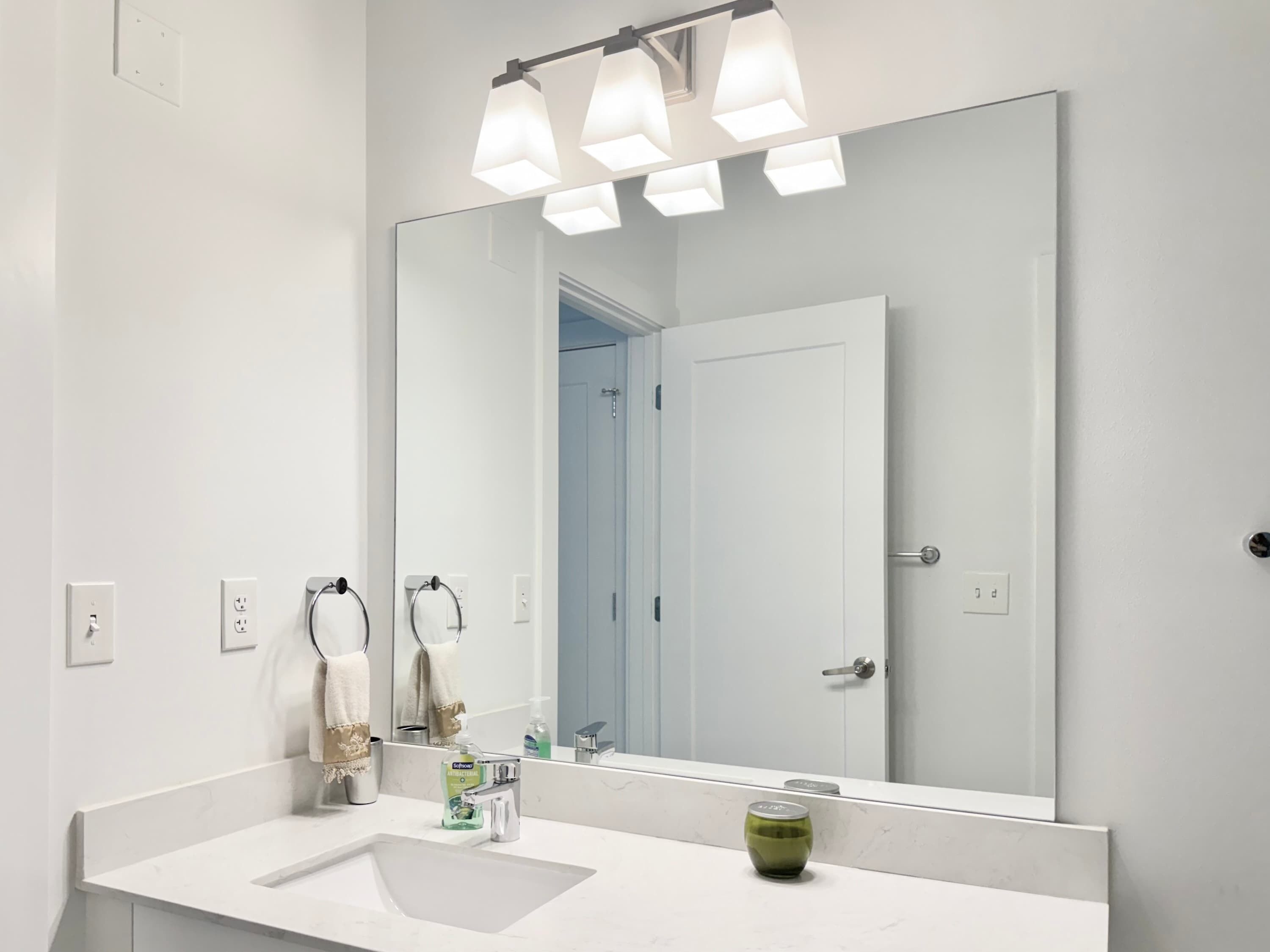 A modern bathroom with a large mirror, white sink, and a green glass on the counter.