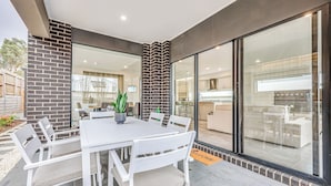 A modern outdoor dining area with a white table and chairs, a potted plant, and a 'WELCOME' mat. - StayAU 5BR Family Getaway GreaterGeelong in Duneed (Mount Duneed)