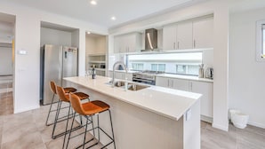 A modern kitchen with a central island, stainless steel appliances, and bar stools. - StayAU 5BR Family Getaway GreaterGeelong in Duneed (Mount Duneed)