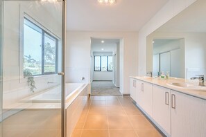 A modern bathroom with a large window, a bathtub, a shower, and a vanity with a mirror.