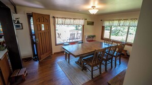 Uma área de refeições com uma mesa e cadeiras de madeira, um tapete e vista para o exterior através de grandes janelas.