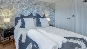 A neatly made bed with a white and blue patterned duvet, a bedside table with a lamp, and a wall with a nature-themed wallpaper.