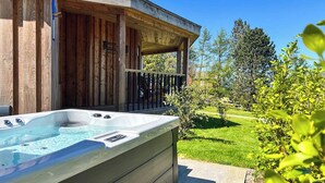 A hot tub outside a wooden building with a covered patio and a grassy yard.