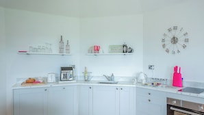 A modern kitchen with white cabinets, a coffee machine, a kettle, and a clock on the wall.