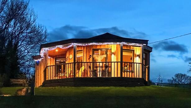 A wooden cabin with a porch, a dining area, and a visible clock.