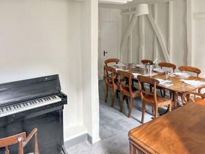 Un coin repas avec un piano, des chaises en bois, une table dressée pour quatre personnes et, au fond, une porte blanche.