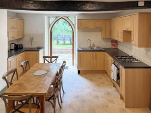 Een moderne keuken met houten kastjes, een eettafel met stoelen, een inbouwfornuis en uitzicht door een groot raam op een terras.