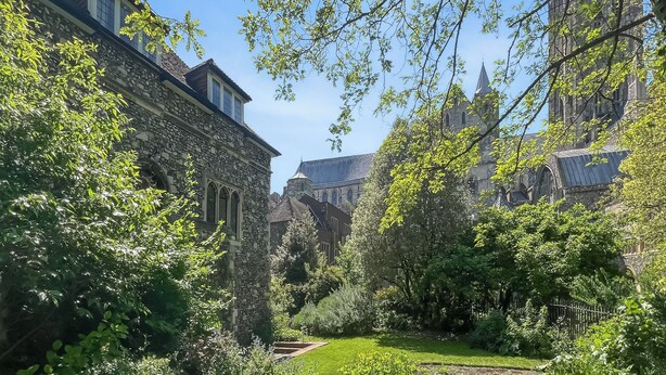 Un edificio histórico con arquitectura de piedra, rodeado de abundante vegetación y un jardín bien cuidado.
