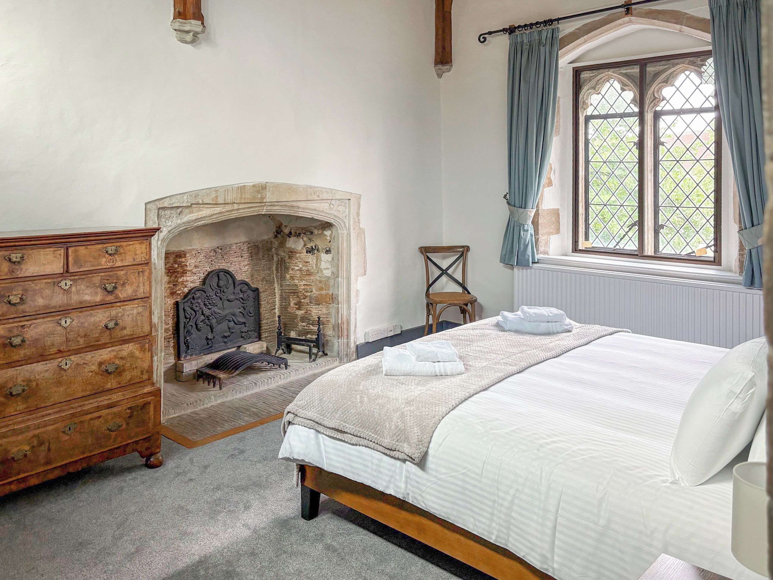 A bedroom with a bed, a dresser, a fireplace, and a window with curtains.