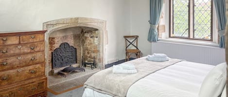 Un dormitorio con cama, cómoda, chimenea y ventana con cortinas.