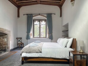 Une chambre à coucher avec un lit en bois, une table de chevet, une lampe, une fenêtre avec des rideaux et une cheminée en pierre.