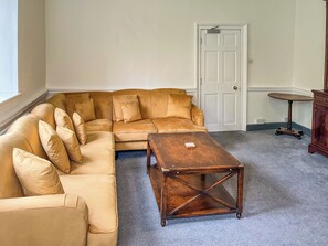Un salon avec un canapé d’angle beige, une table basse en bois, une porte blanche et une petite table ronde.