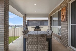 A covered patio with a brick wall, a grill, and wicker furniture. - Ignatius Retreat | Bathurst | Family Entertainer (Kelso)