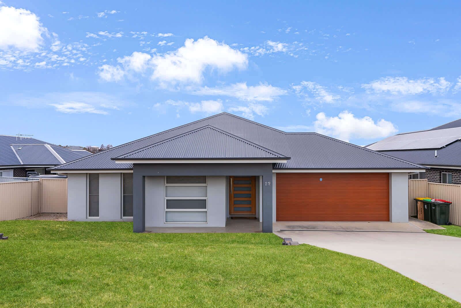 A modern single-story house with a grey roof, a wooden garage door, and a number '22' on the side.