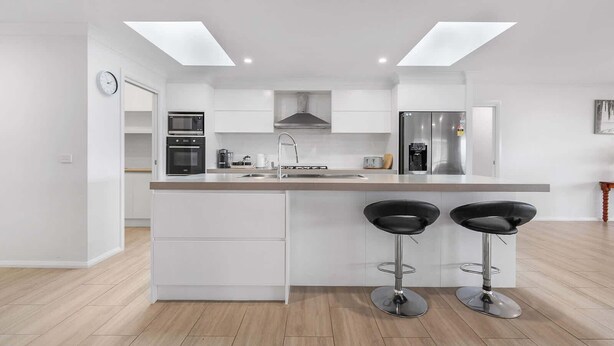 A modern kitchen with white cabinetry, a central island with bar stools, and built-in appliances. - Ignatius Retreat | Bathurst | Family Entertainer (Kelso)