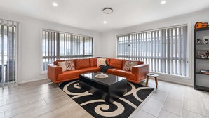 A modern living room with a leather sofa, a glass coffee table, and a black rug. - Ignatius Retreat | Bathurst | Family Entertainer (Kelso)