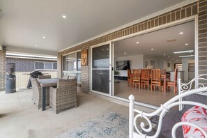A patio with a grill, wicker furniture, and a sliding glass door leading to an interior dining area with wooden chairs and a table. - Ignatius Retreat | Bathurst | Family Entertainer (Kelso)