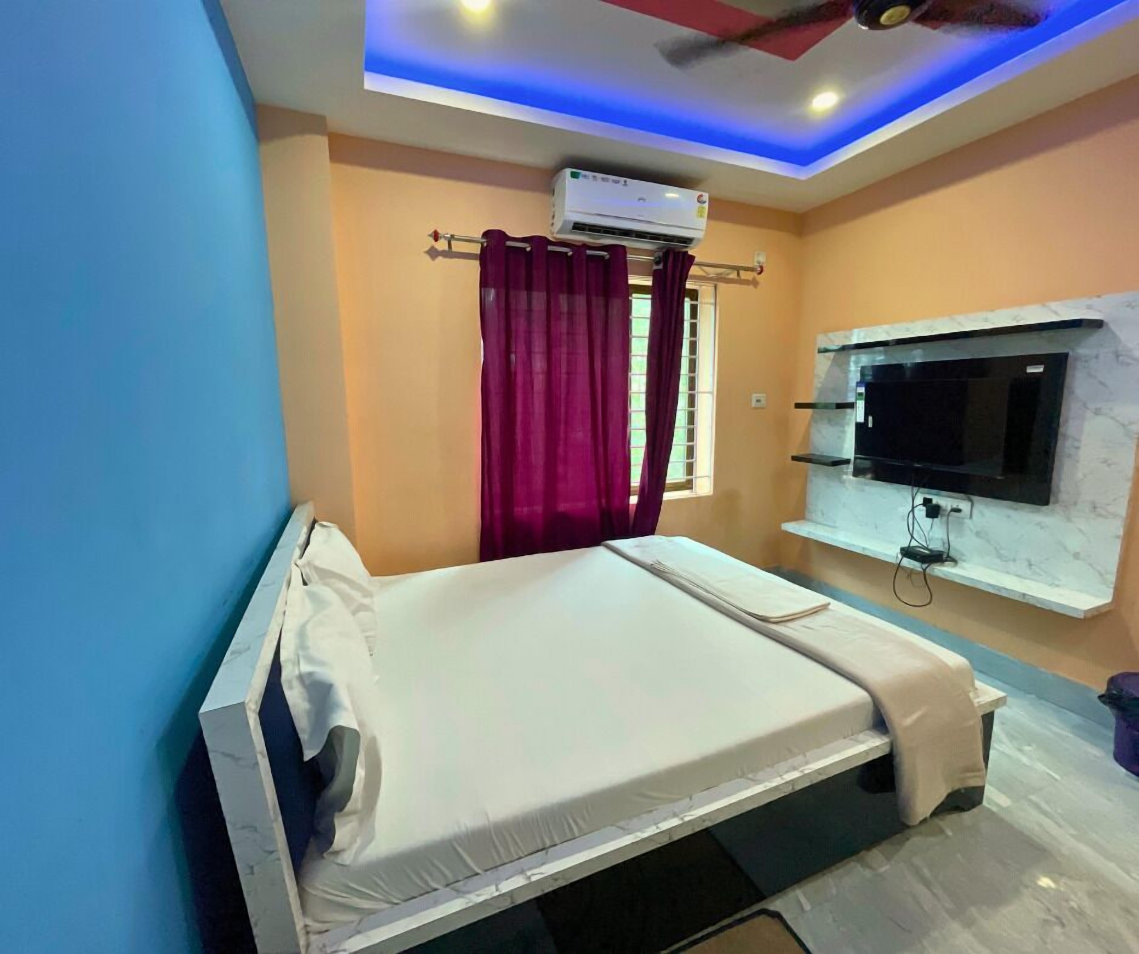 A bedroom with a bed, an air conditioner, a TV mounted on the wall, and a window with curtains.