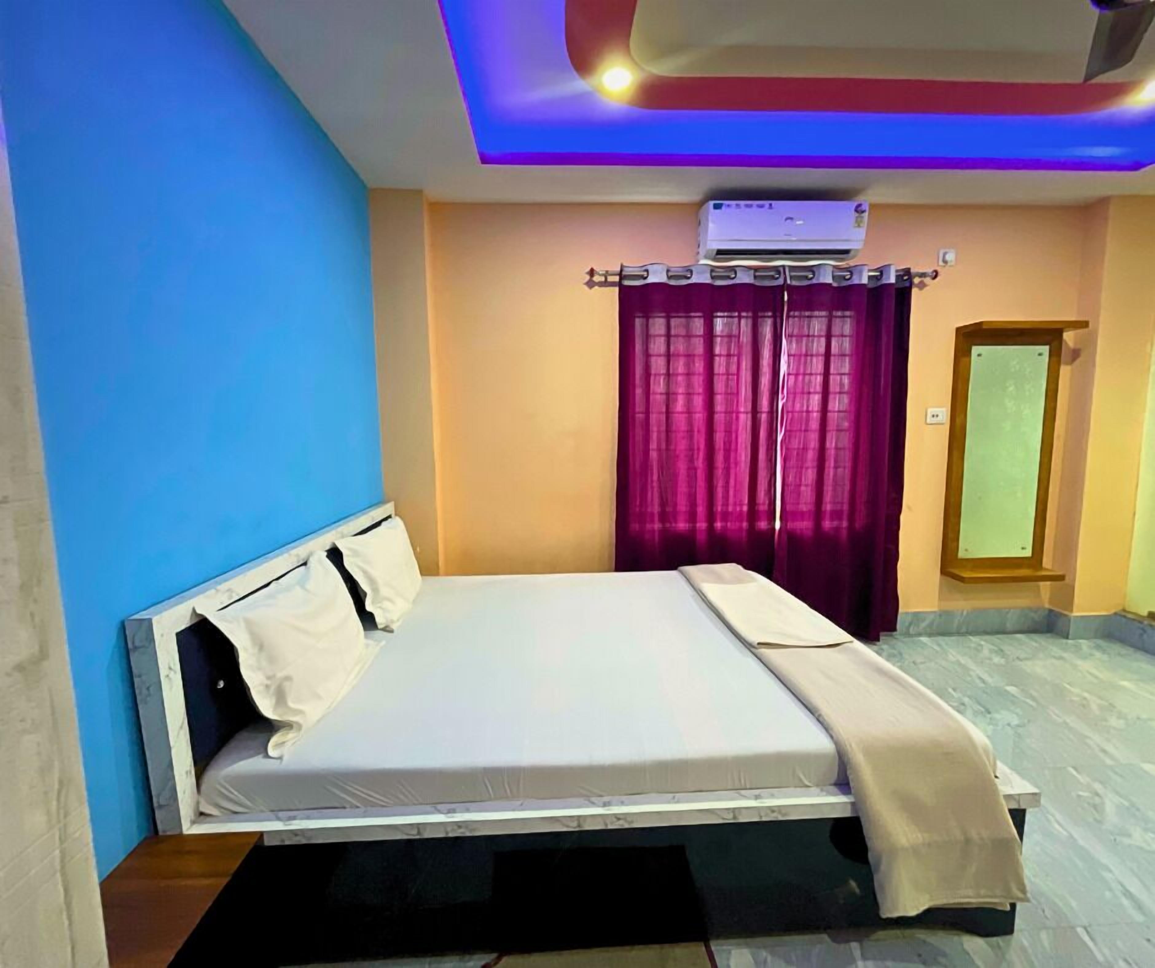 A neatly made bed with a headboard, a window with purple curtains, and an air conditioning unit mounted on the wall.