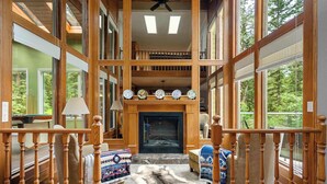 A spacious living room with a fireplace, large windows, and a high ceiling. - Freele Escape | Hot Tub | Nature Lovers Dream! (Priddis)