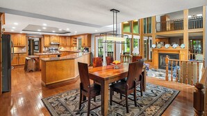 A spacious kitchen with wooden cabinets, a central island, and a dining area with chairs. - Freele Escape | Hot Tub | Nature Lovers Dream! (Priddis)