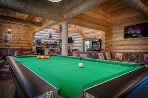 Interior acogedor de una cabaña de troncos con mesa de billar, paredes de madera y televisor.
