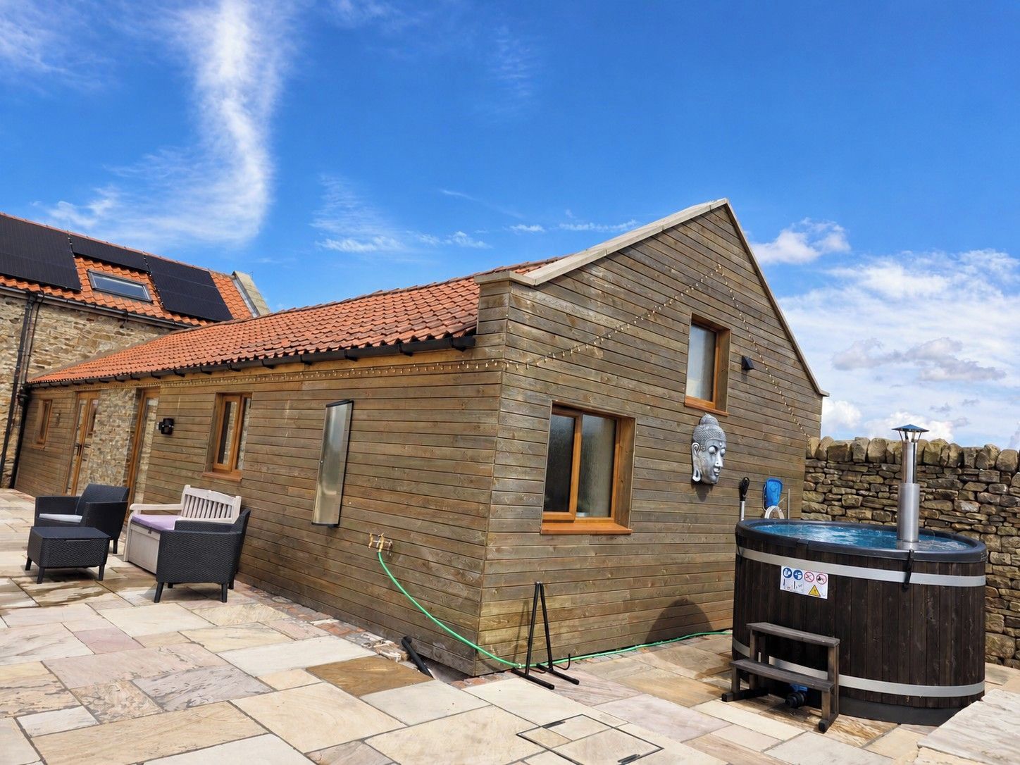 A wooden cabin with a tiled roof, a hot tub, and outdoor seating.
