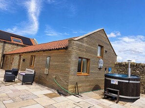 A wooden cabin with a tiled roof, a hot tub, and outdoor seating.