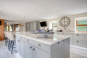 A spacious kitchen with a large island, modern appliances, and a large wall clock.
