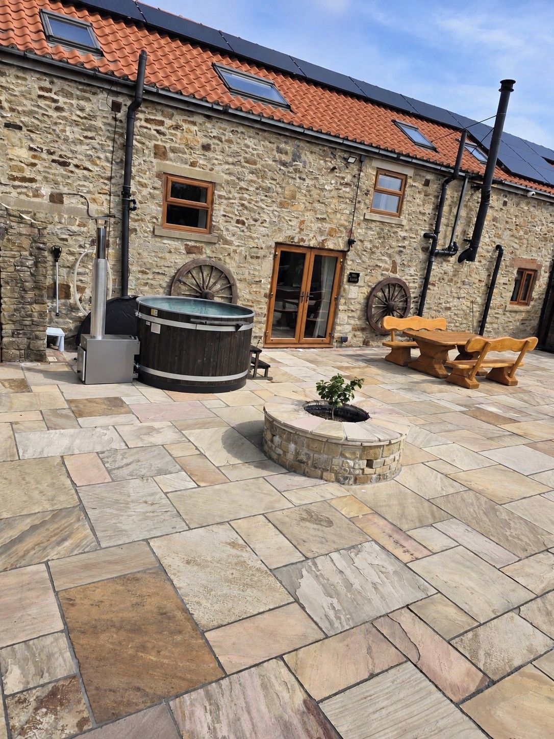 A stone building with a tiled roof, outdoor seating, a hot tub, and a wooden table.