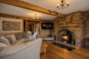A cozy living room with a brick fireplace, wooden beams, and a sectional sofa.