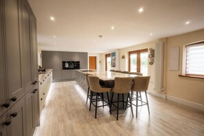 A modern kitchen with a central island, bar stools, and a dining area with a large window.