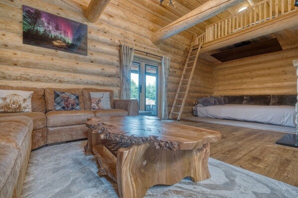 Interior de una cabaña de troncos con una mesa de comedor de madera, un sofá y una cama.