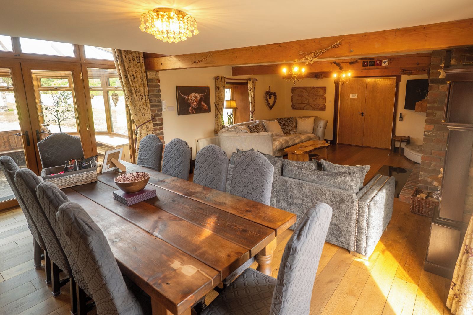 A cozy living room with a wooden dining table, grey upholstered sofas, and a stone fireplace.
